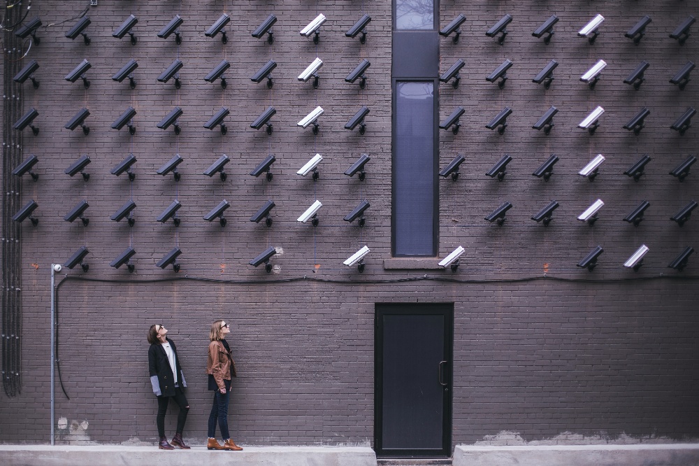 Photo of two people look up at a wall covered in a grid of video cameras